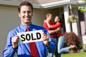 realtor holds sold sign after selling title insurance policy and helping couple reach their commitment to buy a house