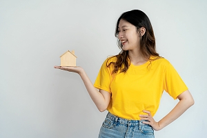 Asian woman wearing yellow shirt holds up small wooden house